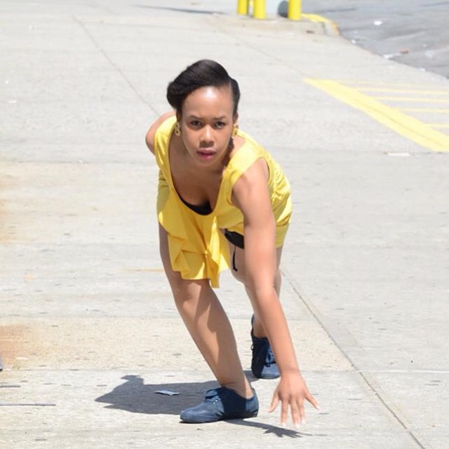 A dancer in a yellow dress looks directly at the contest, looking as if she is about to take off in a sprint